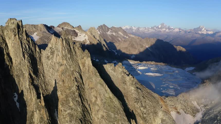 A daytime aerial view of a rocky mountain landscape with snow and ice patches