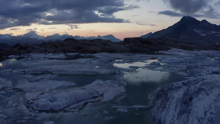 Clouds reflect off ocean water visible between broken glaciers near a mountain range