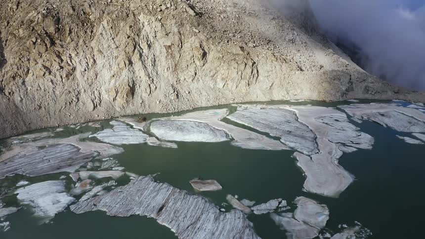 Ice floats on water in valley bordered by dense fog