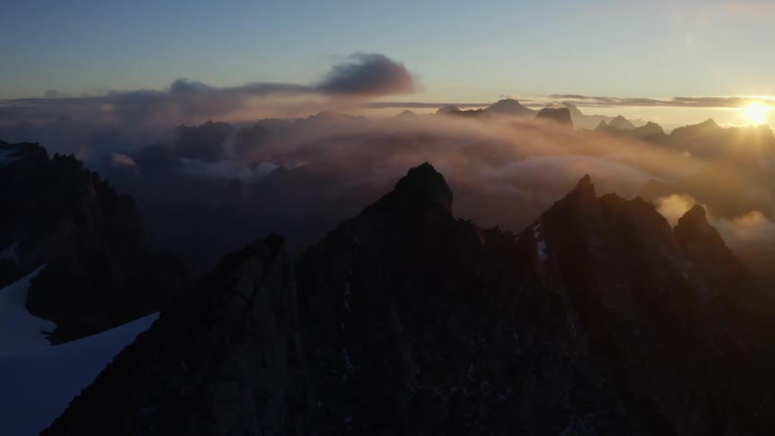 An aerial view of a mountain landscape with clouds and a setting sun at dusk