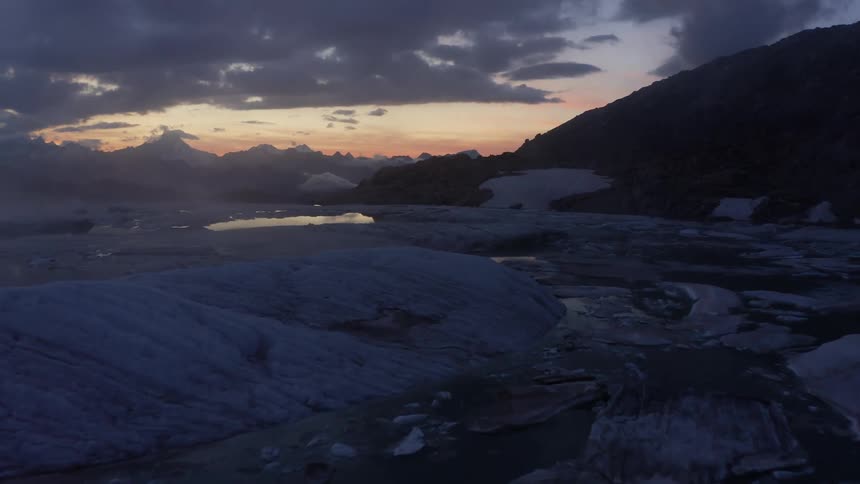 An aerial view of a pool of water and ice on a mountain landscape at dusk