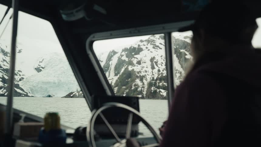 A woman is driving the boat near the snow covered rocks