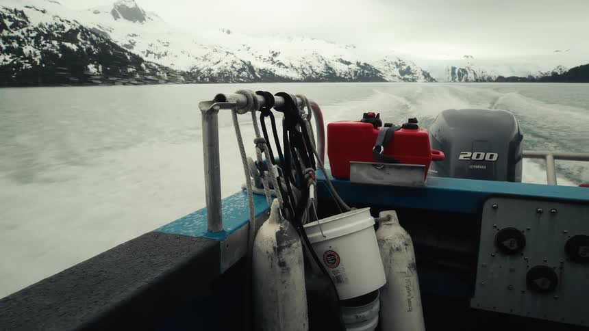 Boat speeds away from shore and snow covered mountains leaving a wake