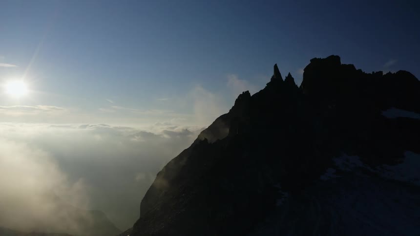 Silhouette of mountain with peaks high in the sky and the sun shining above the clouds