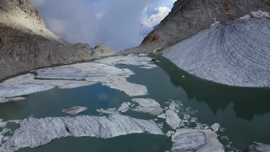 Ice floats of reflective water bordered by steep slopes under a cloudy sky