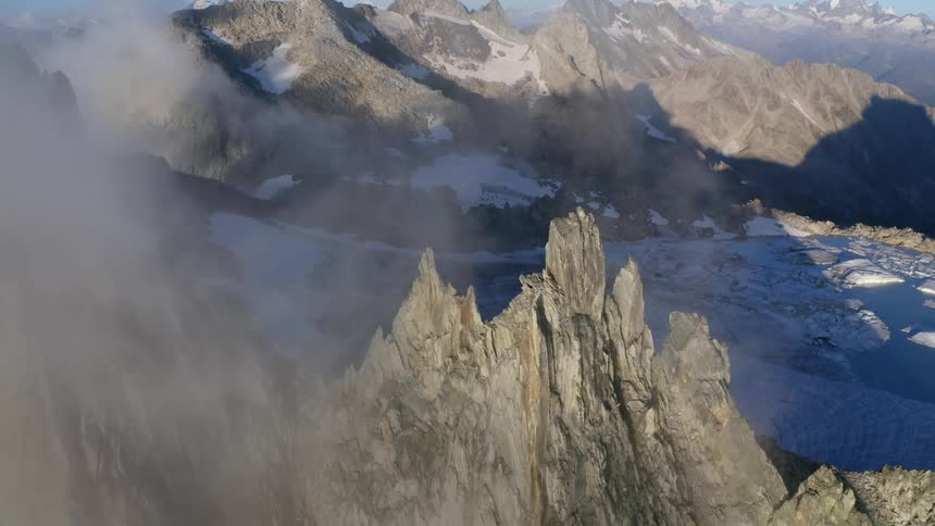 Aerial view of clouds covering the jagged peaks of a mountain range near a lake