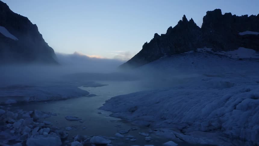 Fog covers river with floating ice that passes between mountains