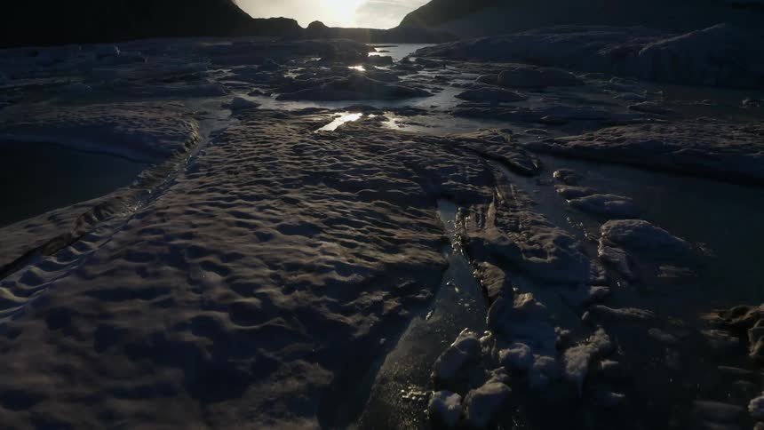 Sunlight shines and reflects off the water and ice surface of a mountain lake
