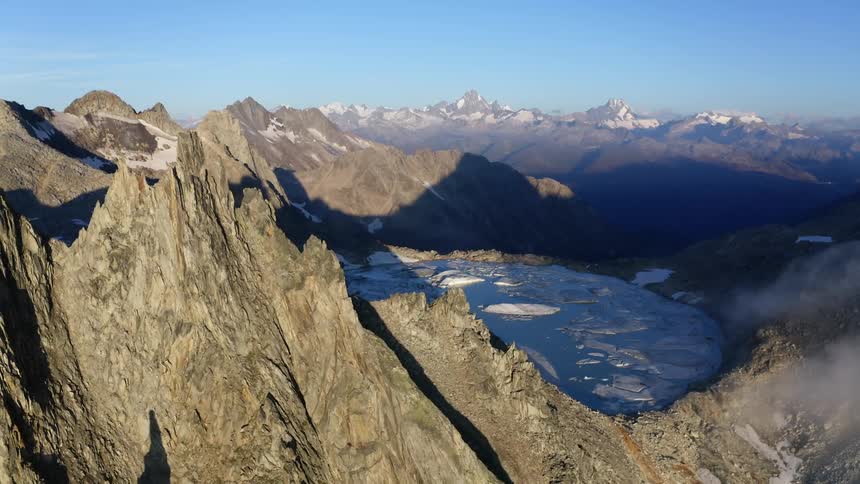 An aerial view of a large pool of water and ice on a jagged rocky mountain landscape in the daytime