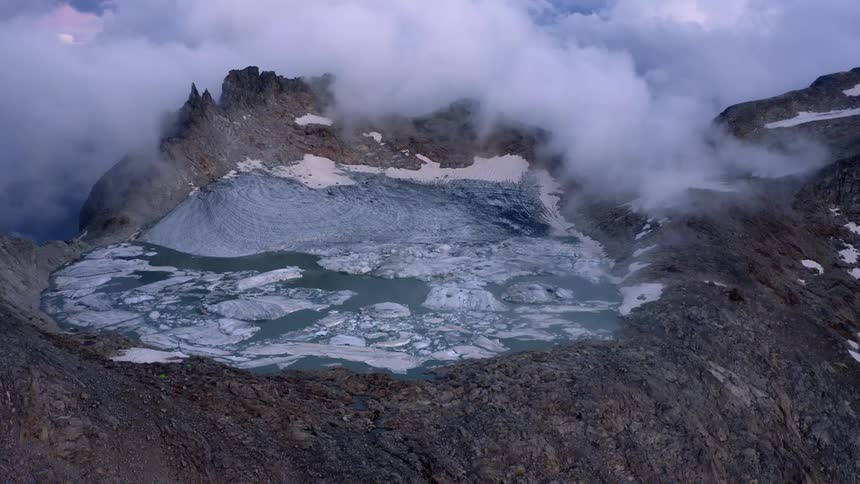Aerial view of a frozen lake atop a mountain under the clouds at evening