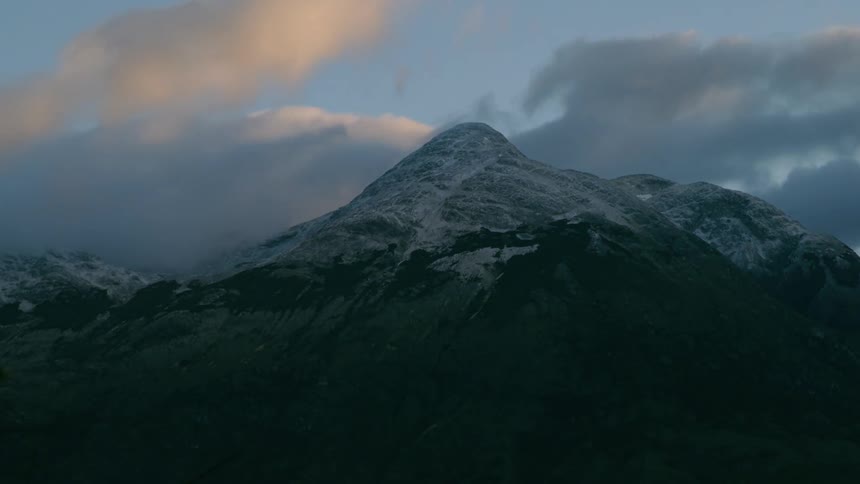 Time Lapse of clouds swirling around a snow covered mountain rising high in the late evening sky