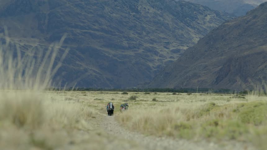 Expedition backpackers journey through a vast and empty valley in the Andes mountains