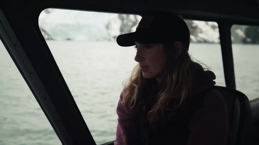 Baseball wearing woman pilots boat across water with snow and ice covered ground in background
