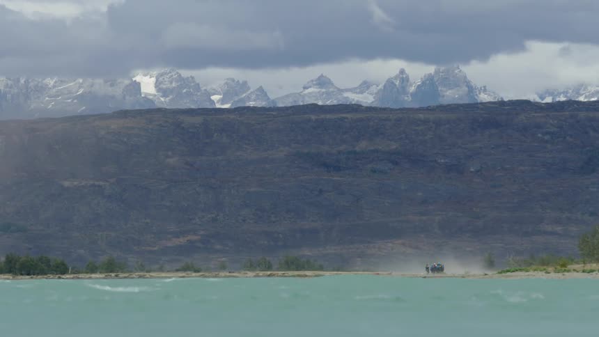 A group of people huddle close together as they withstand windy chaos near windblown rough river waters