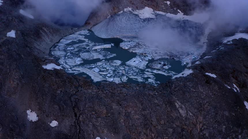 A frozen lake in a mountain top crater with clouds floating above