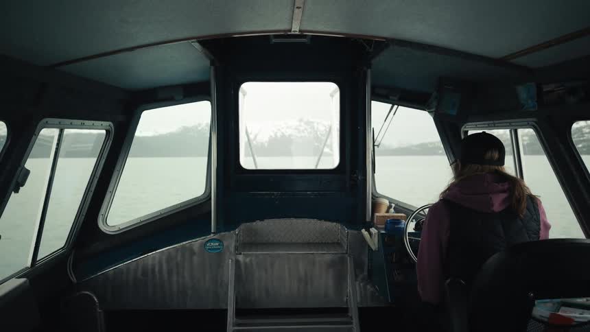 Person pilots boat toward shore and snow covered mountains