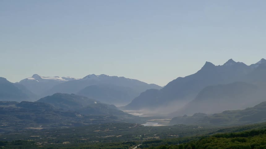 An aerial view of a valley with surrounding mountains on a hazy day