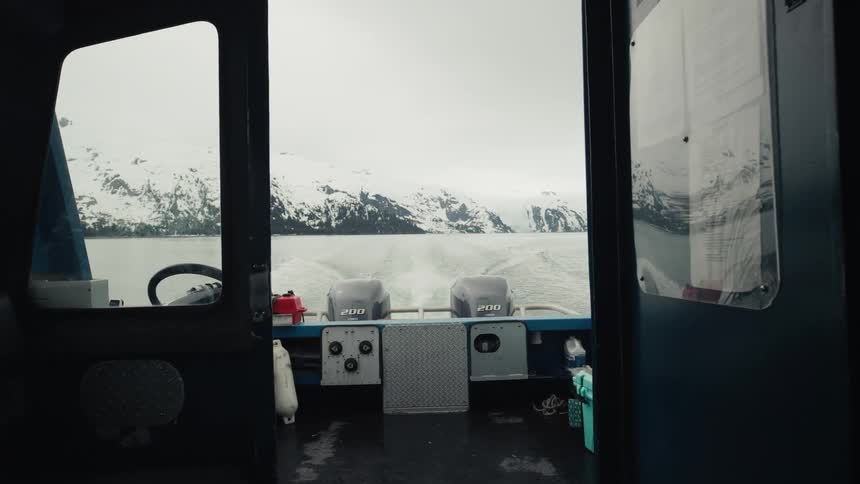 Onboard a large motorboat traveling on a large lake surrounded by snowy mountains on an overcast day