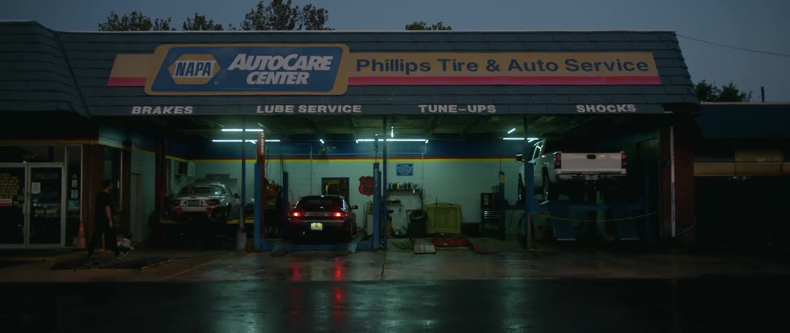 A commercial auto repair shop is working on several vehicles in the evening after a recent rain