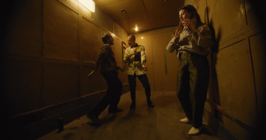 A woman and two men dance in a narrow corridor