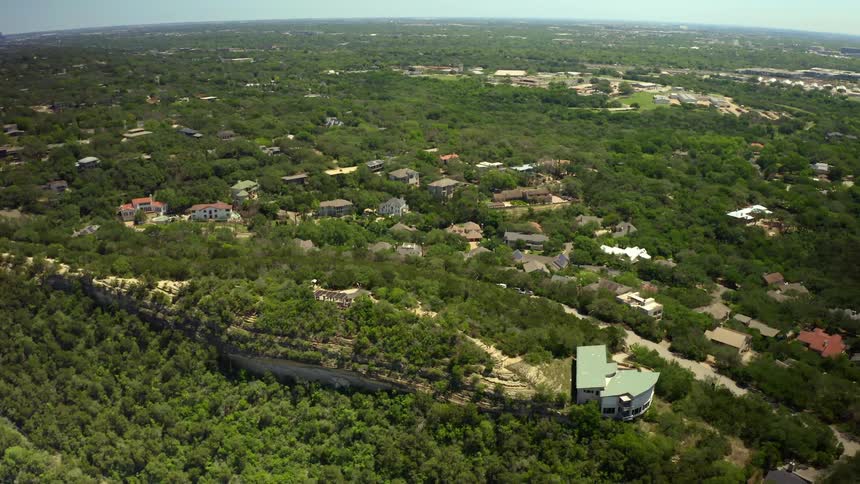 Large house sits on slope near forest surrounded by homes