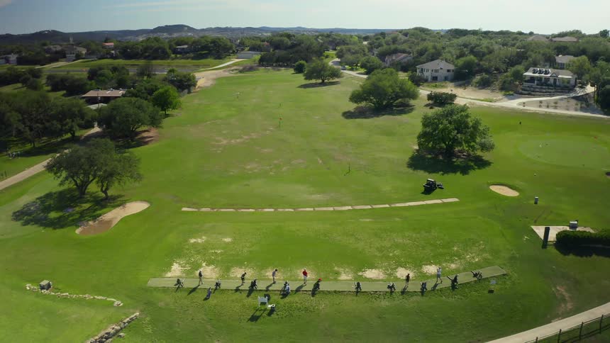 Riding lawn mower moves away from golfers practicing strokes