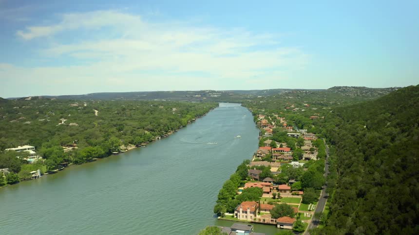 An aerial view of a wealthy suburban neighborhood with hills and lots of trees on a sunny day