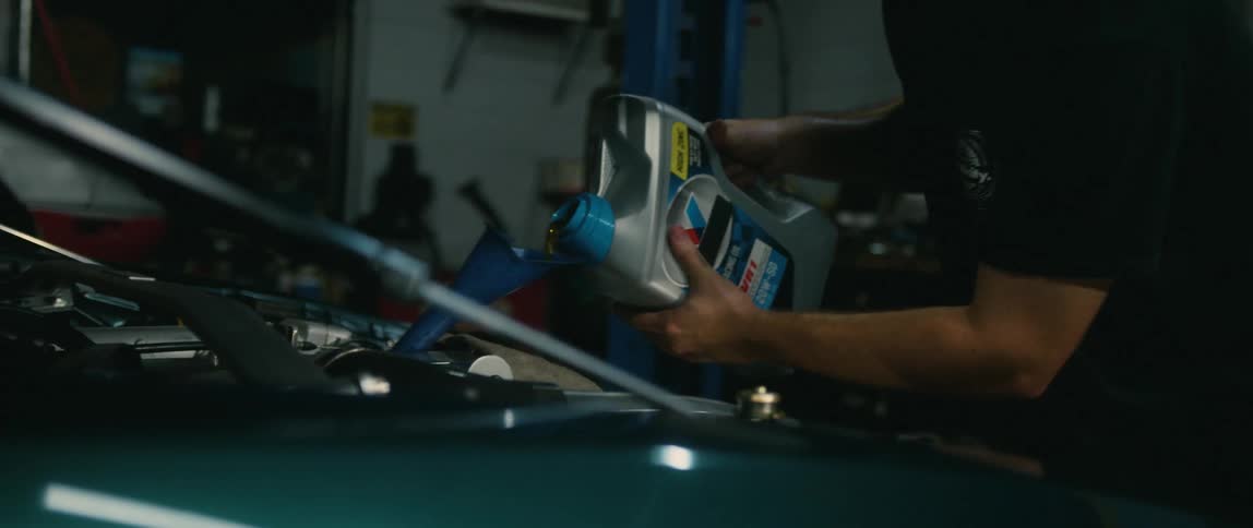 A man pours oil into a funnel in the engine of a car in a garage