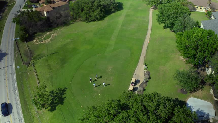 Traffic passes golf course surrounded by homes as golfers move around