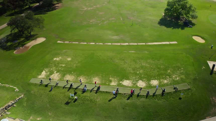 Golfers practice as tractor mows grass