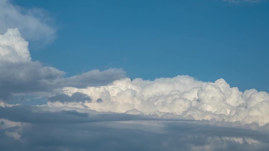 Dense clouds roll and wave in clear blue skies