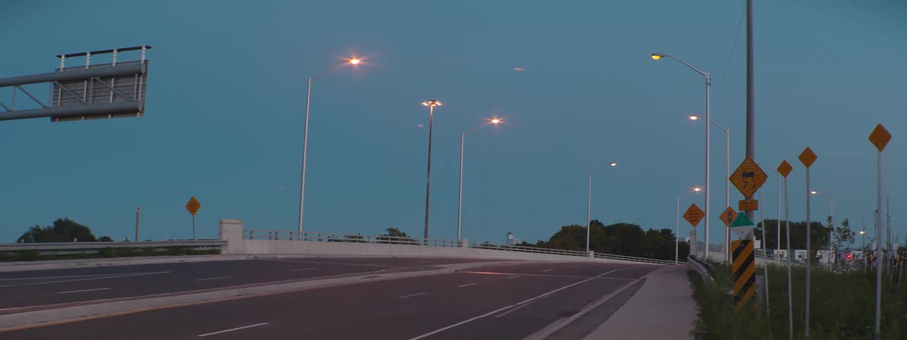 Street lights shine over an empty highway with car lights visible in the distance