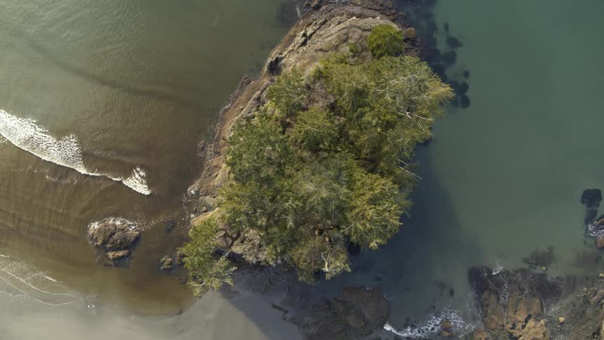 Ascending over a small and tree covered sea stack along a rocky ocean shoreline
