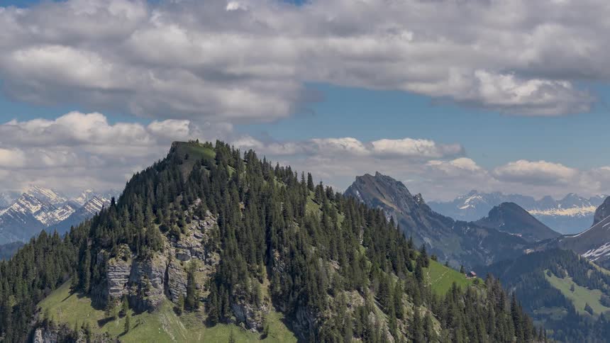 A timelapse aerial view of a mountain and forest landscape with a home located on the mountainside during the day