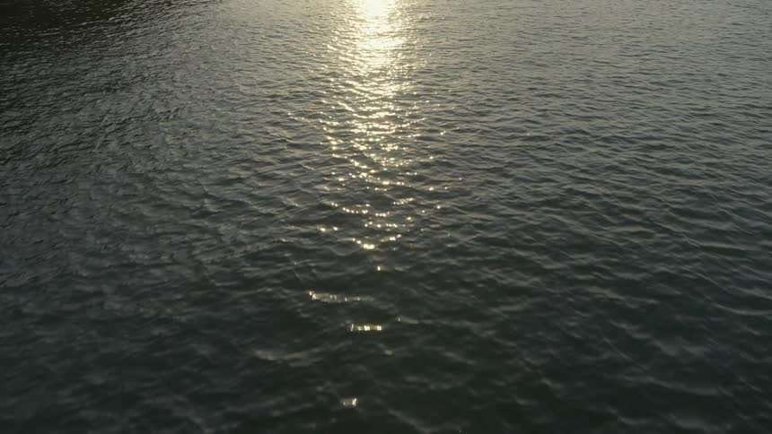 Low traverse over calm ocean water as the sun reflects from its surface