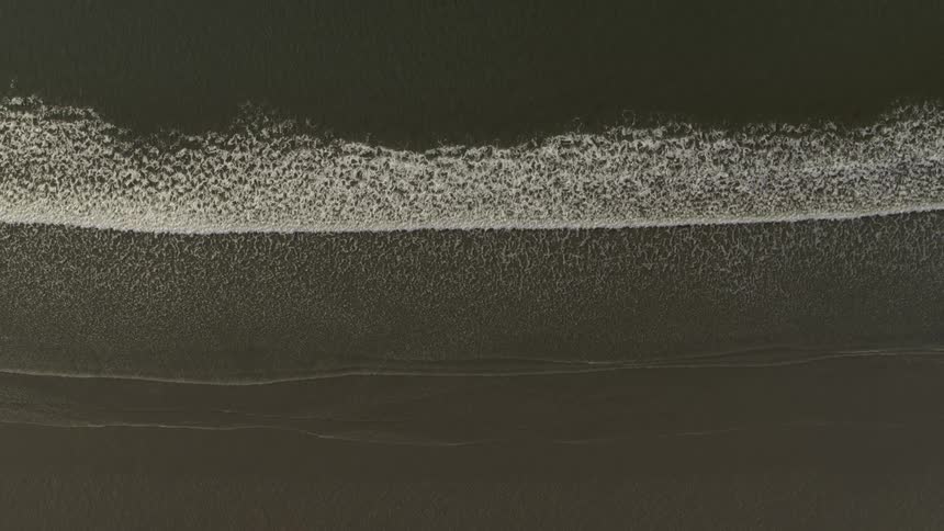 Rapid rise above ocean waves washing onto an empty and pristine sandy beach