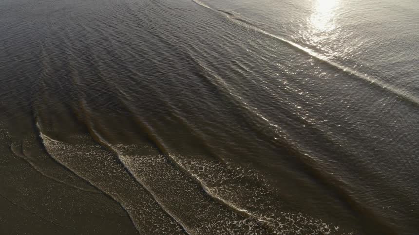 Gentle waves wash ashore as the sun relects along calm ocean water
