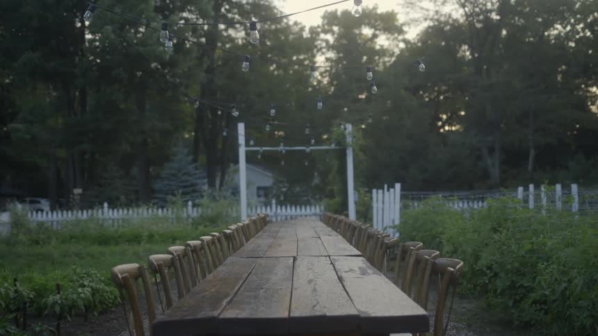 A long wooden table surrounded by chairs sits in a yard