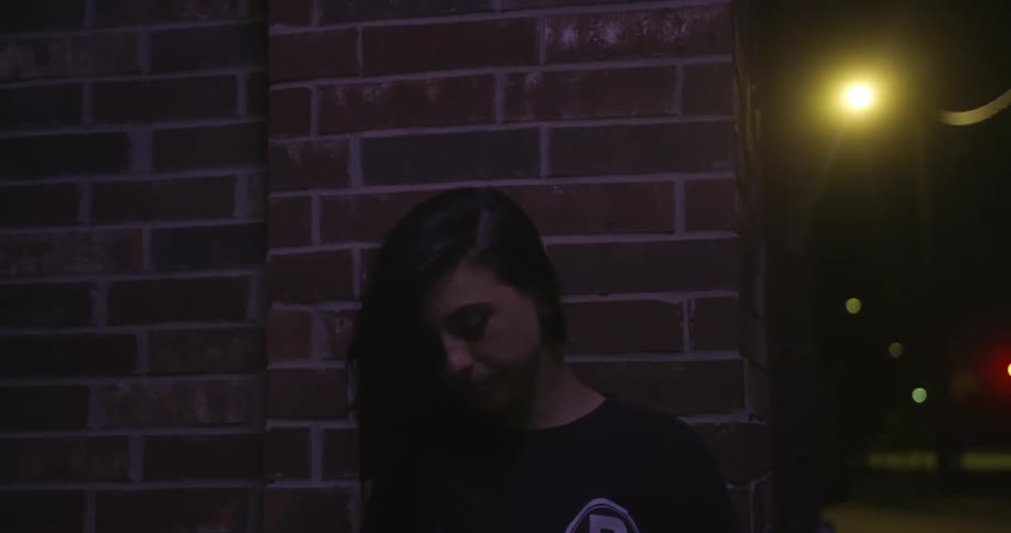 A woman is leaning against a brick wall at night