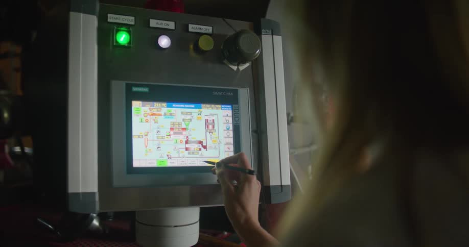 A woman uses a stylus on a touch screen display panel then pushes a flashing green button