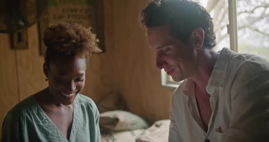 A man and woman look at a tablet together while sitting in a room filled with burlap sacks