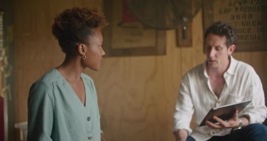 A woman smells coffee beans while chatting with a colleague holding a tablet