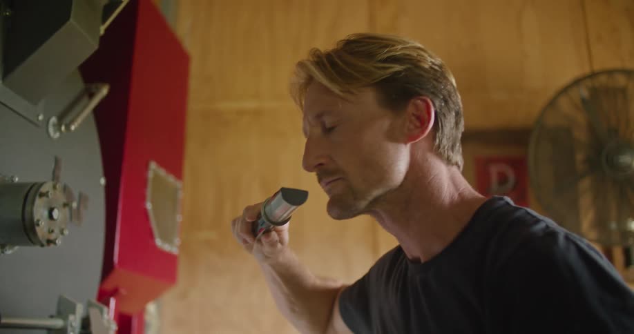 A man removes a small scoop from a machine and sniffs it