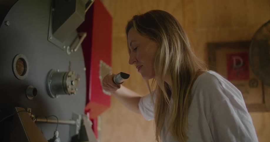 A woman pulls a scoop out of an industrial roaster to smell the aroma of the coffee beans
