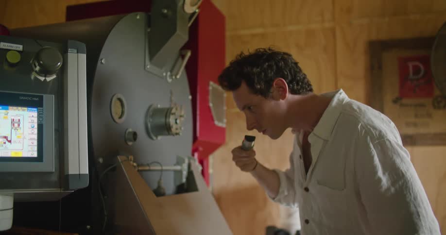 A man pulls a scoop of coffee beans out of the roaster to check the aroma