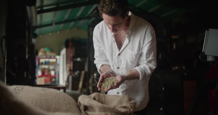 A man runs his hands through a large sack of coffee beans in the back of a shop