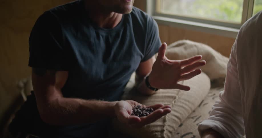 Man with white shirt and blonde man wearing dark blue t shirt check coffee beans and talk about business in coffee warehouse