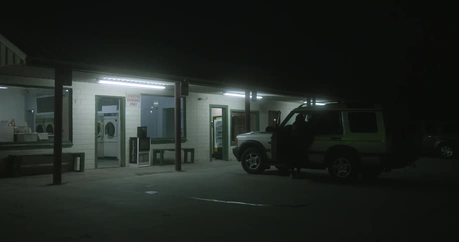 A woman exits a building with a basket and puts it in a car