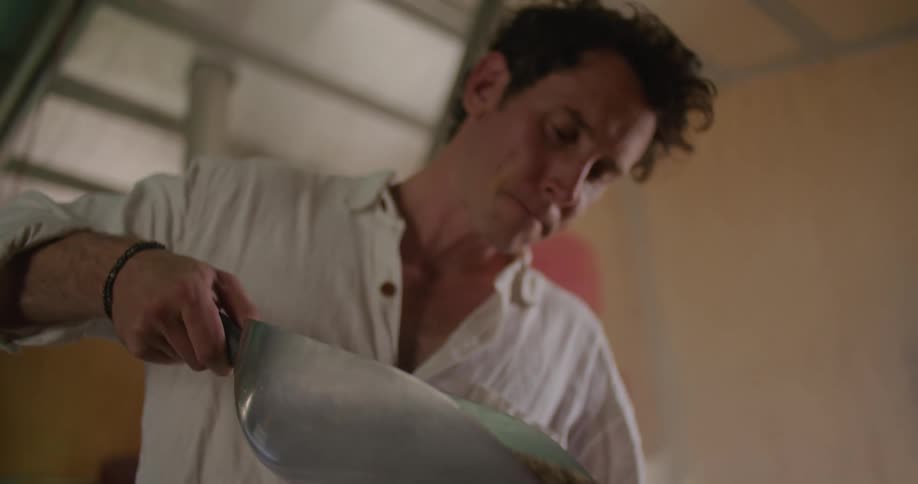 A man pours coffee beans out of a large metal scoop