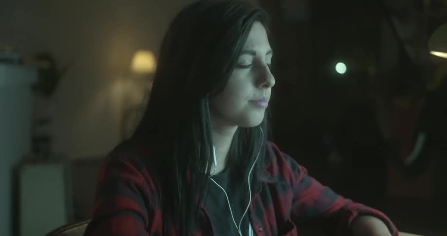 A woman closes her eyes in a room with blinking lights while listening to music